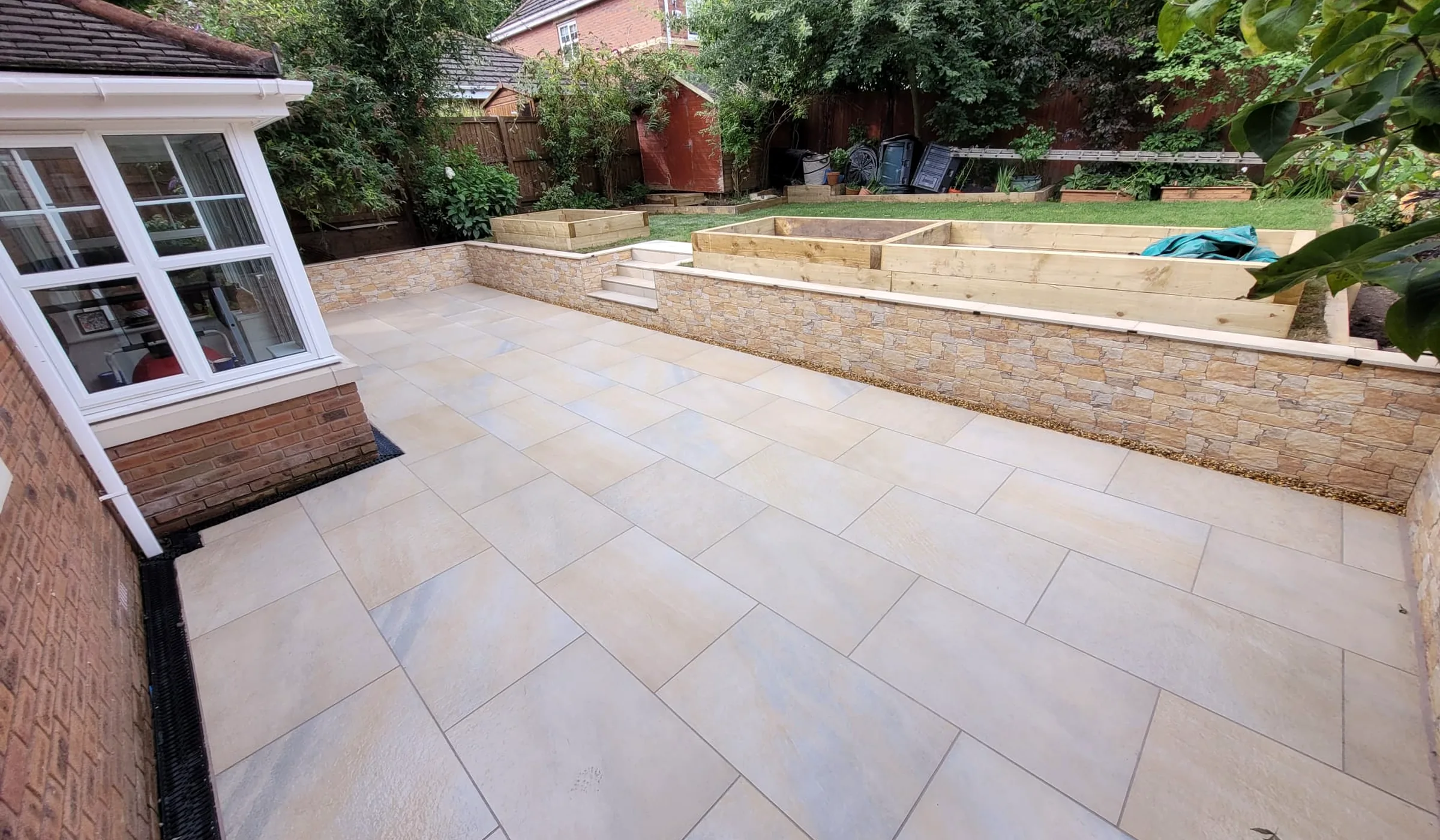 Completed porcelain patio with tiered retaining walls, steps and raised garden beds